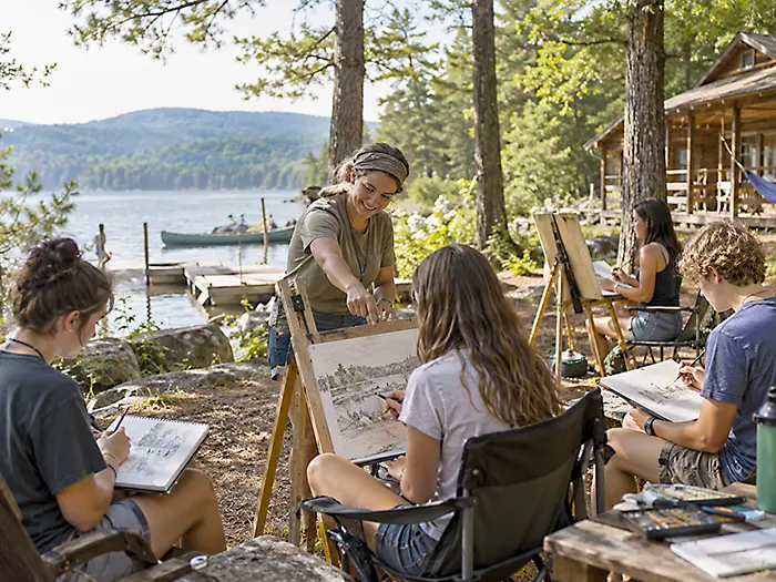 Teens sketching with an art instructor beside a lake at summer Art Camp